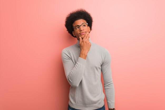 Jeune homme afro-américain sur un mur rose doutant et confus