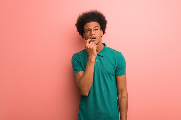 Jeune homme afro-américain sur un mur rose doutant et confus