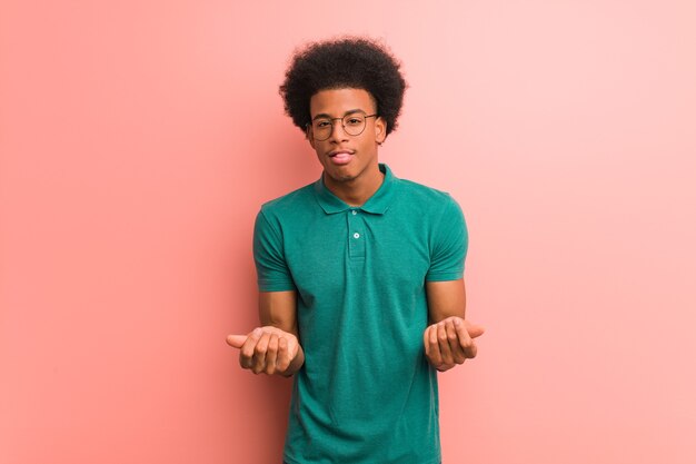 Jeune homme afro-américain sur un mur rose faisant un geste de besoin