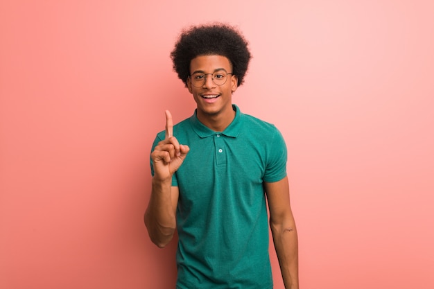 Jeune homme afro-américain sur un mur rose montrant le numéro un