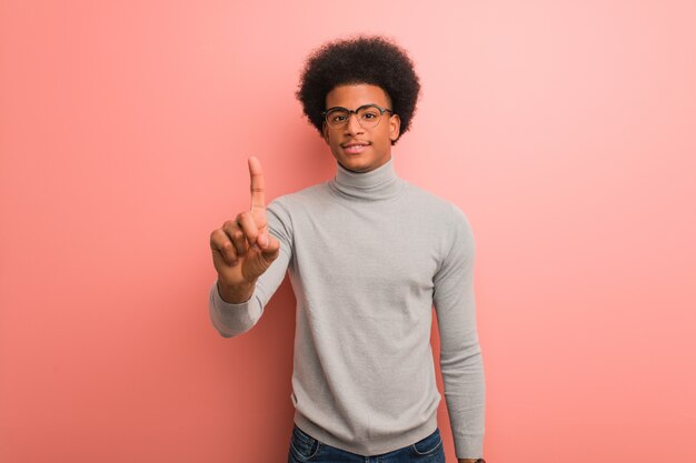 Jeune homme afro-américain sur un mur rose montrant le numéro un