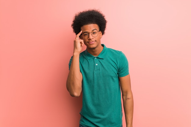 Jeune homme afro-américain sur un mur rose en pensant à une idée