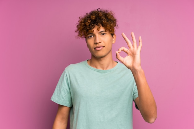 Jeune homme afro-américain sur mur violet isolé, montrant un signe ok avec les doigts