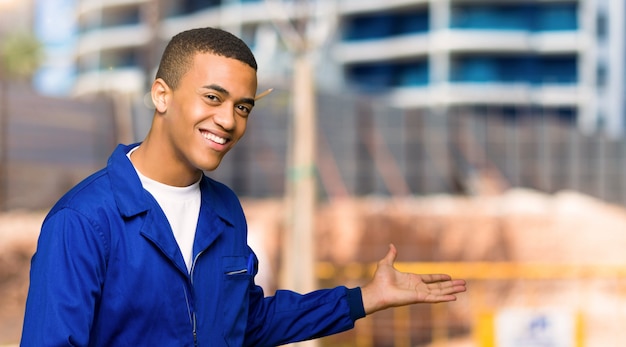 Jeune Homme Afro-américain Ouvrier Pointant En Arrière Et Présentant Un Produit Sur Un Chantier De Construction