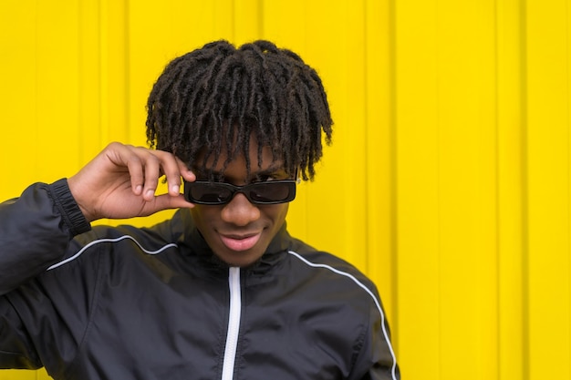 Jeune homme afro-américain portant des lunettes de soleil avec une attitude cool à côté d'un mur urbain jaune