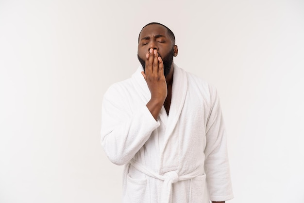 Jeune homme afro-américain portant un peignoir sur fond blanc isolé pensant avoir l'air fatigué et ennuyé par des problèmes de dépression