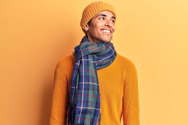 Jeune homme afro-américain portant des vêtements d'hiver décontractés regardant de côté avec le sourire sur le visage, expression naturelle. rire confiant.