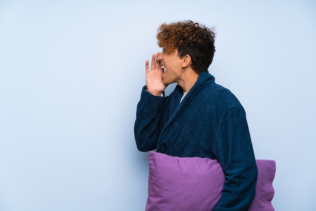 Jeune homme afro-américain en pyjama criant avec la bouche grande ouverte