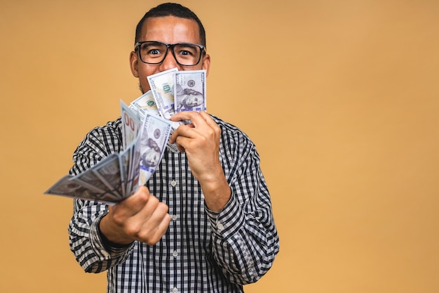 Jeune homme afro-américain riche en t-shirt décontracté tenant des billets d'un dollar avec surprise