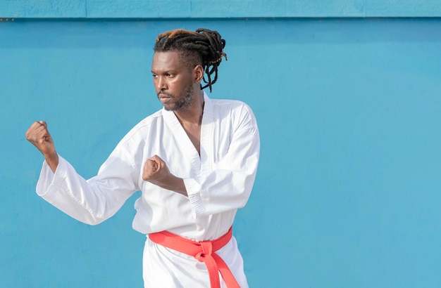 Un jeune homme afro-américain s'entraînant au taekwondo à l'extérieur sur fond bleu