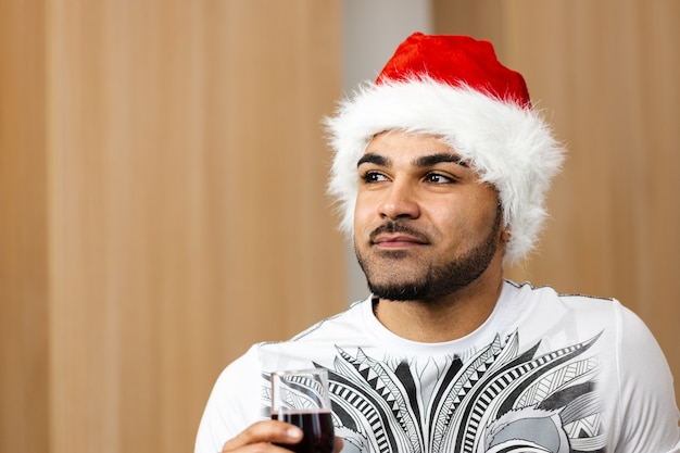 Jeune homme afro-américain à santa cap buvant du vin rouge