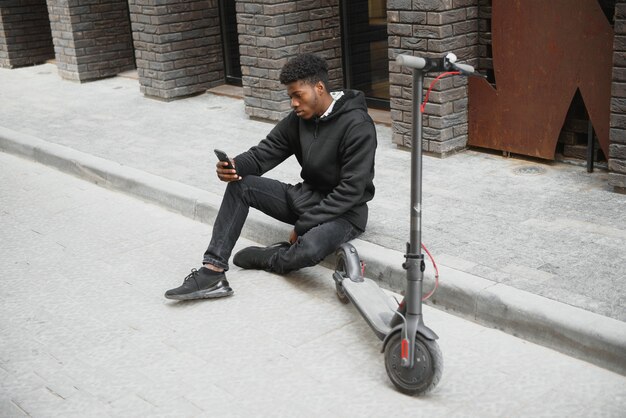 Jeune homme afro-américain avec scooter électrique dans la ville
