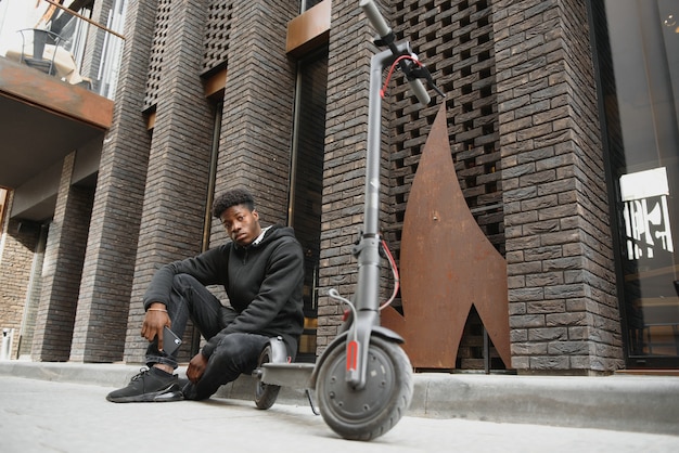 Jeune homme afro-américain avec scooter électrique dans la ville