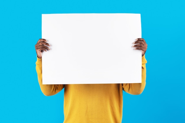 Photo jeune homme afro-américain se cachant le visage derrière une pancarte blanche vierge