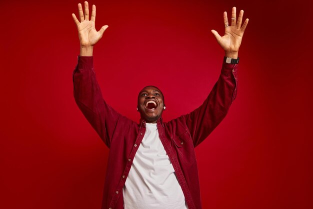 jeune homme afro-américain se réjouit avec les mains à la caméra isolé sur fond rouge portrait de studio