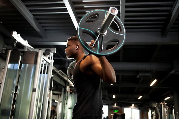 Un jeune homme afro-américain soulève des haltères dans un gymnase sombre, un gars sportif s'entraîne dans la salle de fitness