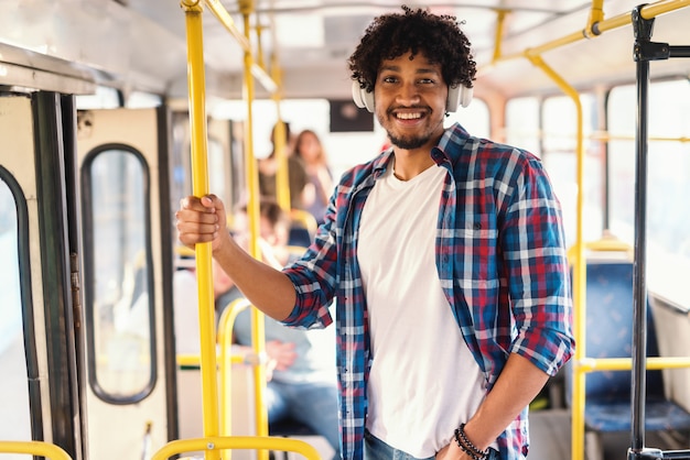 Jeune homme afro-américain souriant conduisant dans les transports publics et écoutant de la musique tout en tenant la poignée.