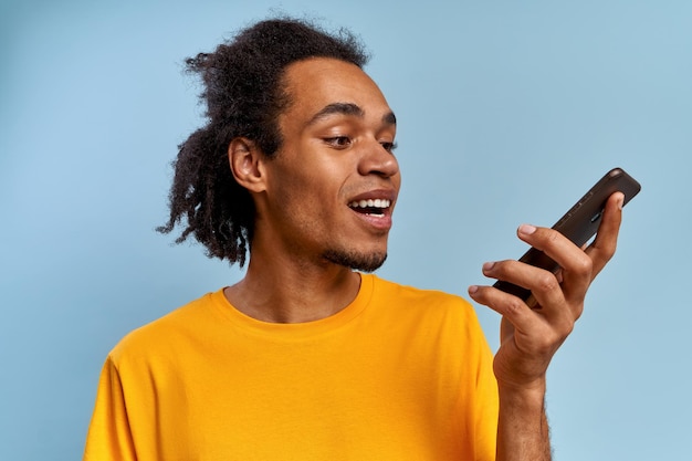 Jeune homme afro-américain souriant positif parlant sur smartphone