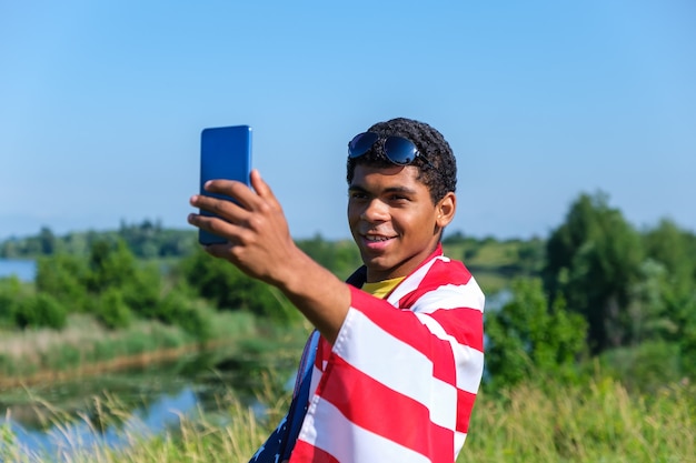 Jeune homme afro-américain souriant recouvert de drapeau américain prenant selfie