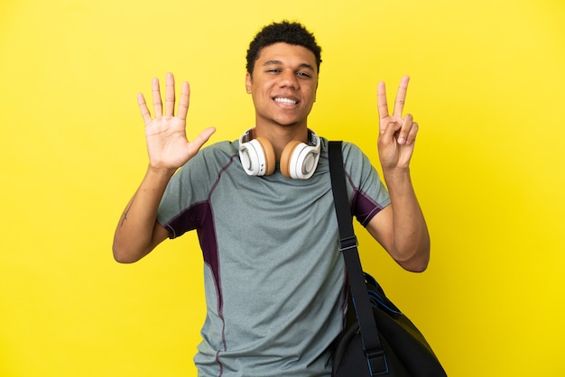 Jeune homme afro-américain de sport avec sac de sport isolé sur fond jaune comptant sept avec les doigts