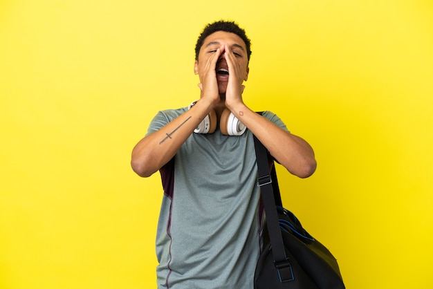 Jeune homme afro-américain de sport avec sac de sport isolé sur fond jaune criant et annonçant quelque chose