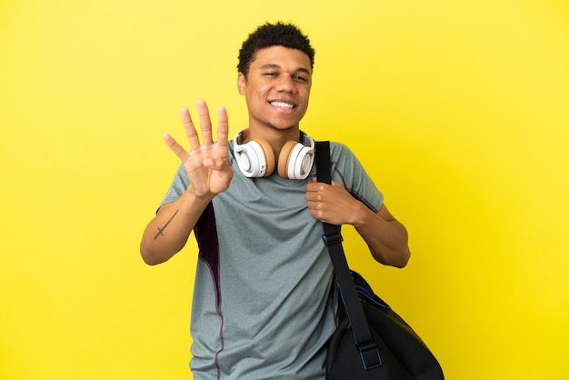 Jeune homme afro-américain de sport avec sac de sport isolé sur fond jaune heureux et comptant quatre avec les doigts