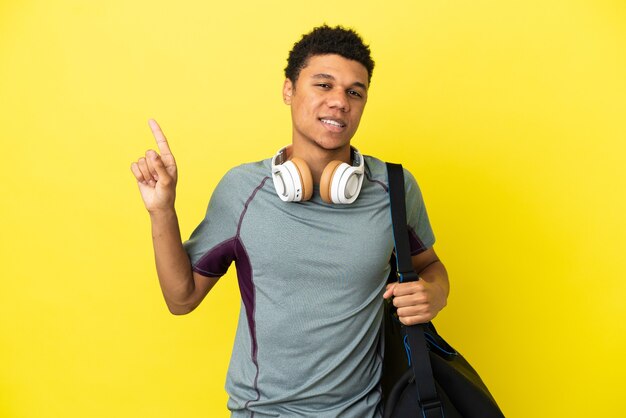 Jeune homme afro-américain de sport avec sac de sport isolé sur fond jaune montrant et levant un doigt en signe du meilleur