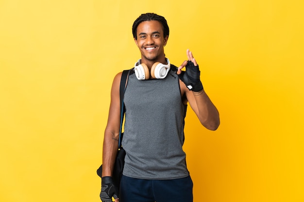 Jeune homme afro-américain de sport avec des tresses avec sac isolé sur fond jaune montrant signe ok avec les doigts