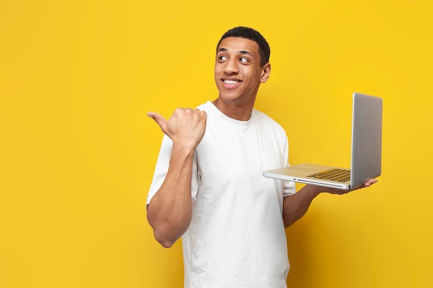 Jeune homme afro-américain en t-shirt blanc utilise un ordinateur portable et montre avec sa main sur l'espace de copie