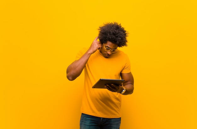 Jeune homme afro-américain avec une tablette contre orange