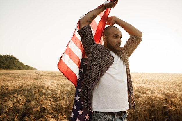 Jeune homme afro-américain tenant le drapeau national des États-Unis à travers le champ de blé