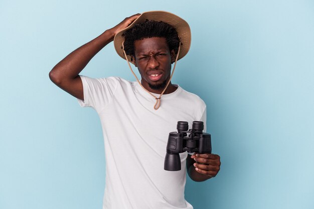 Jeune homme afro-américain tenant des jumelles isolées sur fond bleu étant choqué, elle s'est souvenue d'une réunion importante.