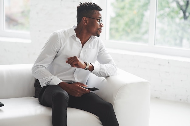 Jeune homme afro-américain en tenue de bureau assis sur le canapé blanc