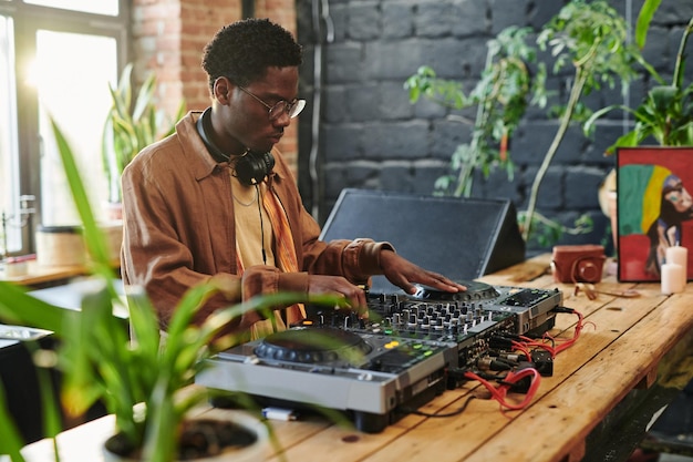 Jeune homme afro-américain tournant des mélangeurs et des platines d'équipement dj