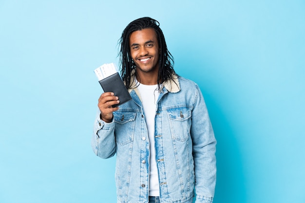 Jeune homme afro-américain avec des tresses sur bleu heureux en vacances avec passeport et billets d'avion
