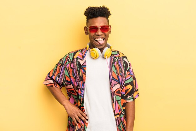 Jeune homme afro noir avec une attitude joyeuse et rebelle plaisantant et tirant la langue avec des lunettes de soleil et des écouteurs