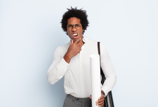 Jeune homme afro noir avec la bouche et les yeux grands ouverts et la main sur le menton, se sentant désagréablement choqué, disant quoi ou wow