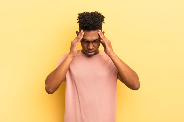 Jeune homme afro noir qui a l'air stressé et frustré de travailler sous pression avec un mal de tête et troublé par des problèmes