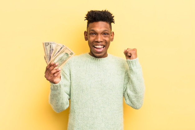 Photo jeune homme afro noir se sentant choqué en riant et célébrant le concept de billets de banque en dollars succès