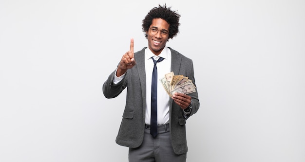 Jeune homme afro noir souriant fièrement et avec confiance en faisant le numéro un pose triomphalement, se sentant comme un leader