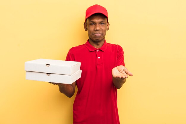 Jeune homme afro noir souriant joyeusement avec amical et offrant et montrant un concept concept de livreur de pizza