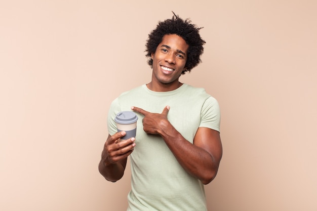 Jeune homme afro noir souriant joyeusement, se sentant heureux et pointant vers le côté et vers le haut, montrant l'objet dans l'espace de copie