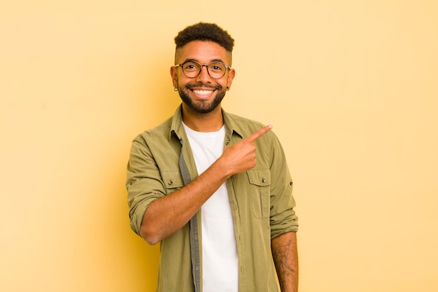 Jeune homme afro à la recherche excité et surpris pointant vers le côté et vers le haut pour copier l'espace