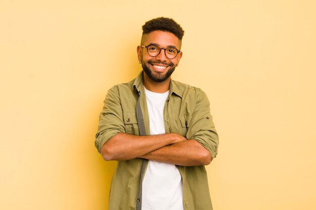 Jeune homme afro ressemblant à un réalisateur heureux, fier et satisfait, souriant avec les bras croisés