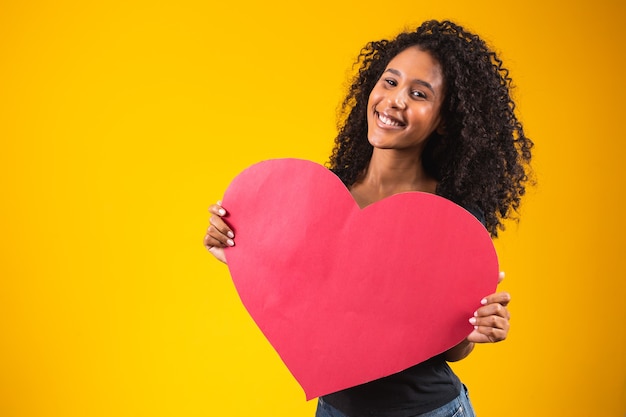 Jeune homme afro séduisant montrant un coeur rouge sur fond jaune.