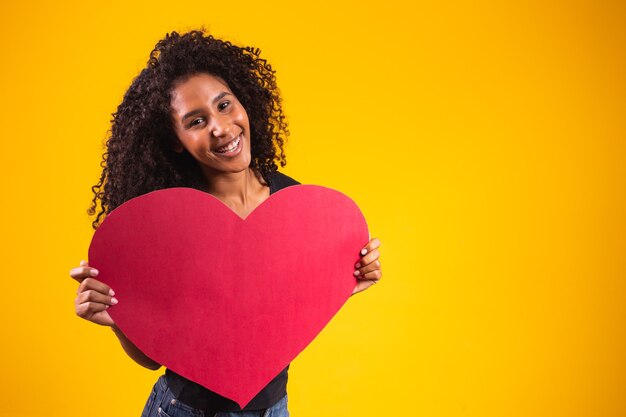 Jeune homme afro séduisant montrant un coeur rouge sur fond jaune.