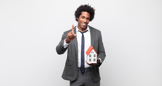 Photo jeune homme afro souriant fièrement et en toute confiance faisant numéro un. concept de l'état réel