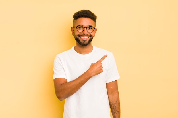 Jeune homme afro souriant joyeusement se sentant heureux et pointant vers le côté et vers le haut montrant l'objet dans l'espace de copie