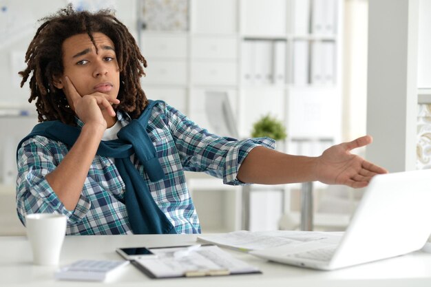 Photo jeune homme afro travaillant au bureau, utilisant un ordinateur portable