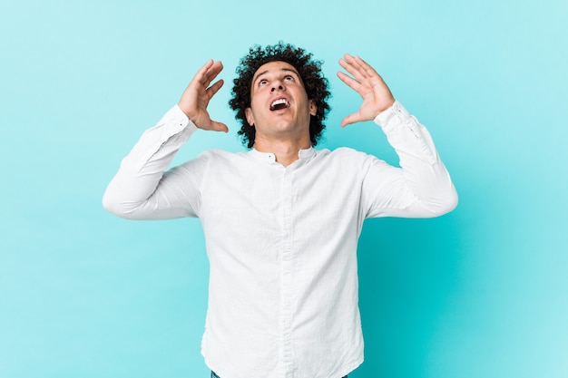 Jeune homme d'âge mûr bouclé portant une chemise élégante criant vers le ciel, levant les yeux, frustré.